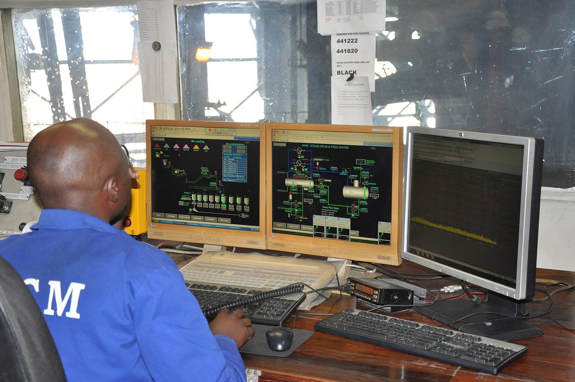 An operator at a plant control room desk watching SCADA process screens
